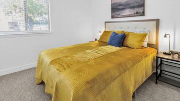A hotel room with a large bed, a nightstand, a lamp, and a painting on the wall.