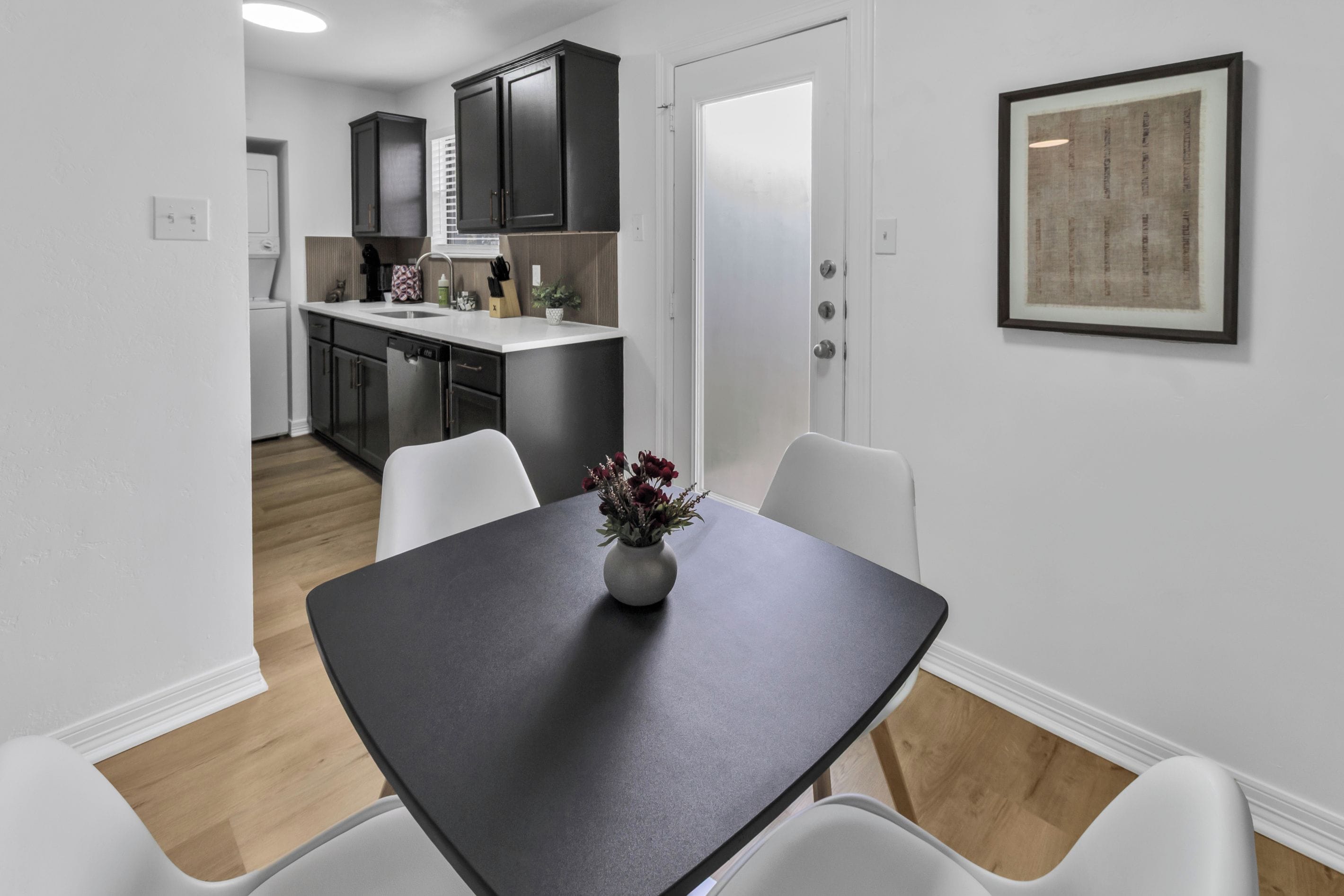A modern kitchen with dark cabinets, a white countertop, and a dining area with a dark table and white chairs.
