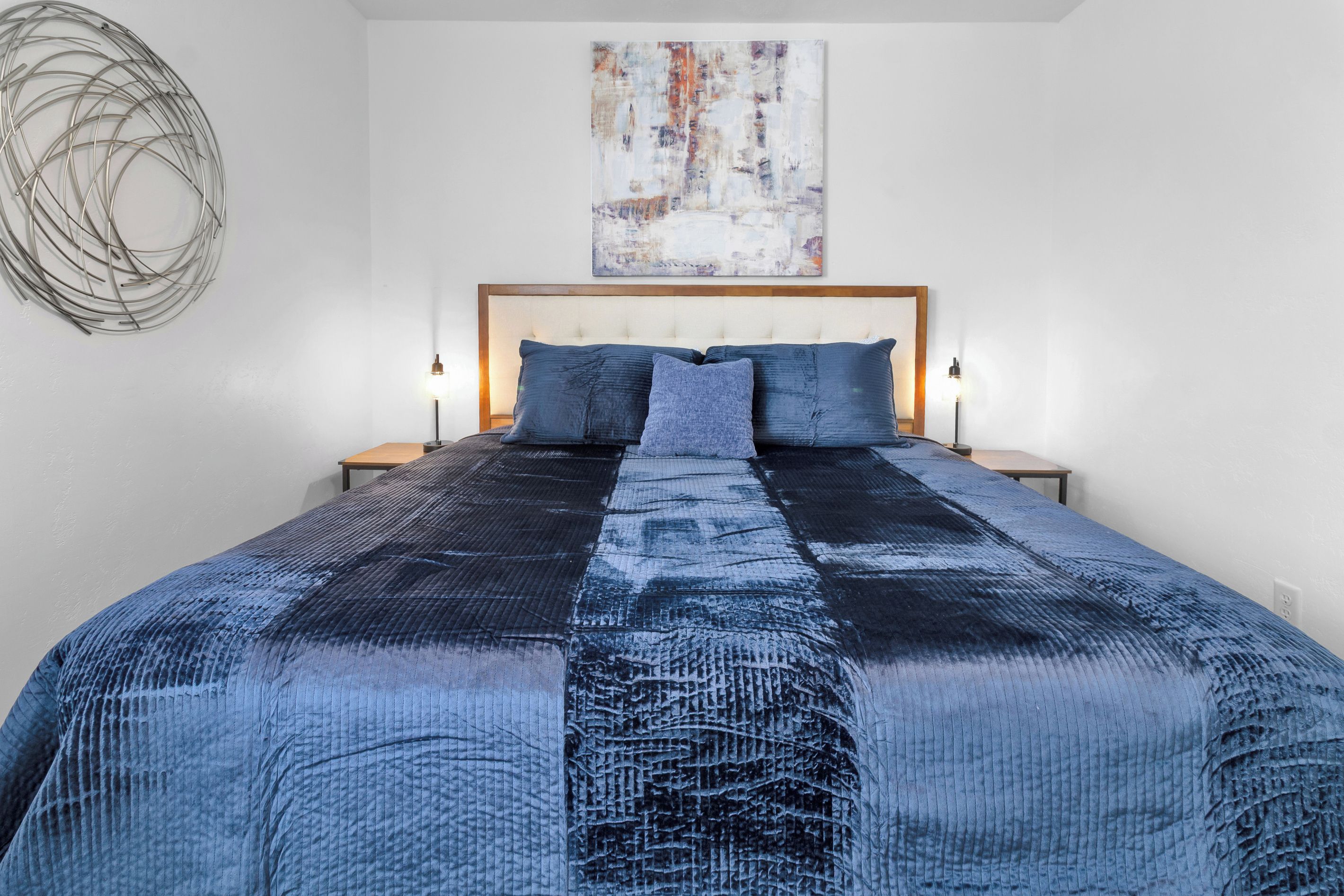 Een slaapkamer met een groot bed, twee nachtkastjes, een abstract schilderij aan de muur, en een bijzondere ronde decoratie.