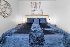 Une chambre à coucher avec un grand lit, deux tables de chevet, un tableau abstrait accroché au mur et un élément de décoration murale circulaire original.