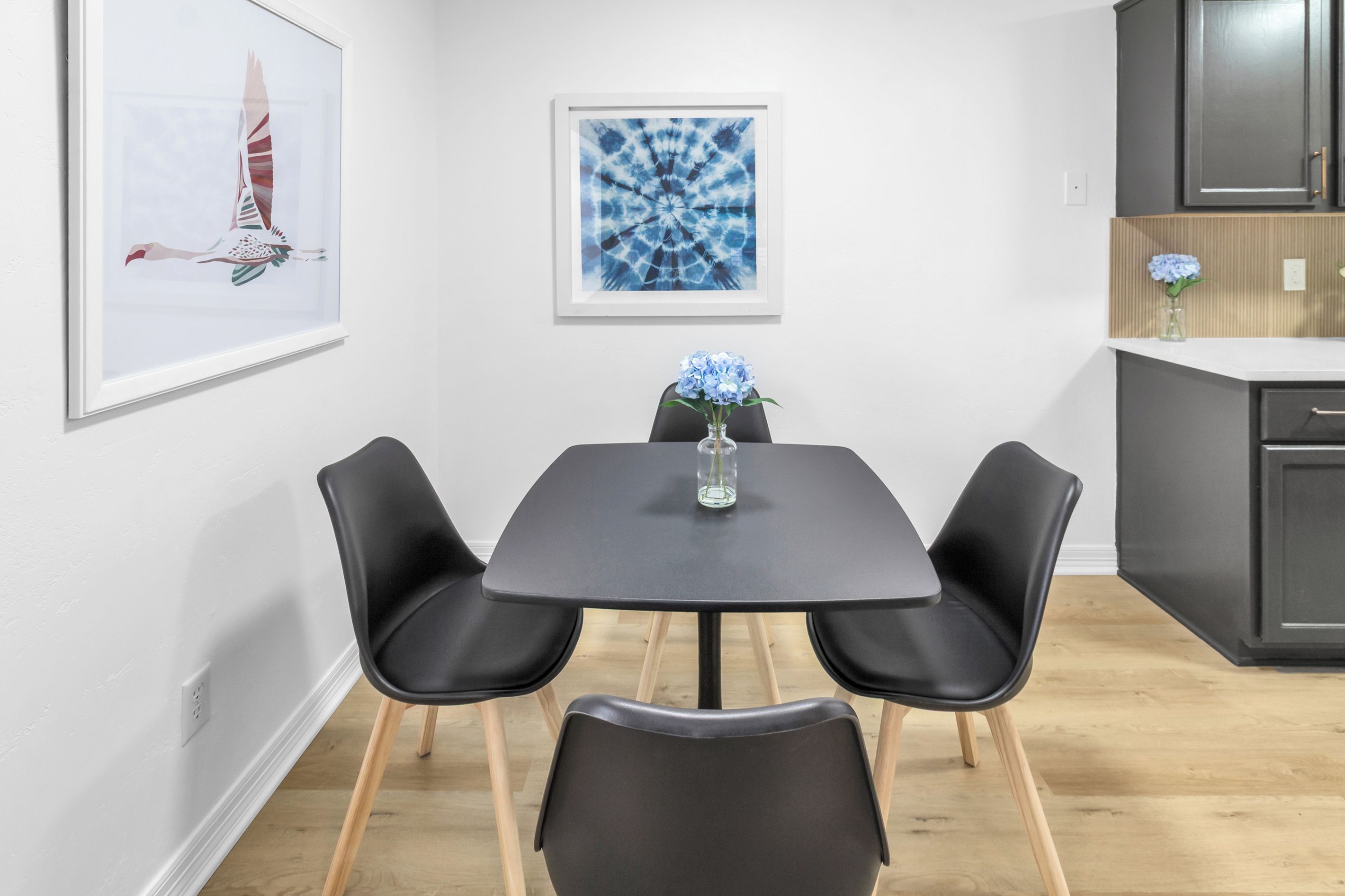 Een eetruimte met een tafel, vier stoelen en twee kunstwerken in lijsten aan de muur.
