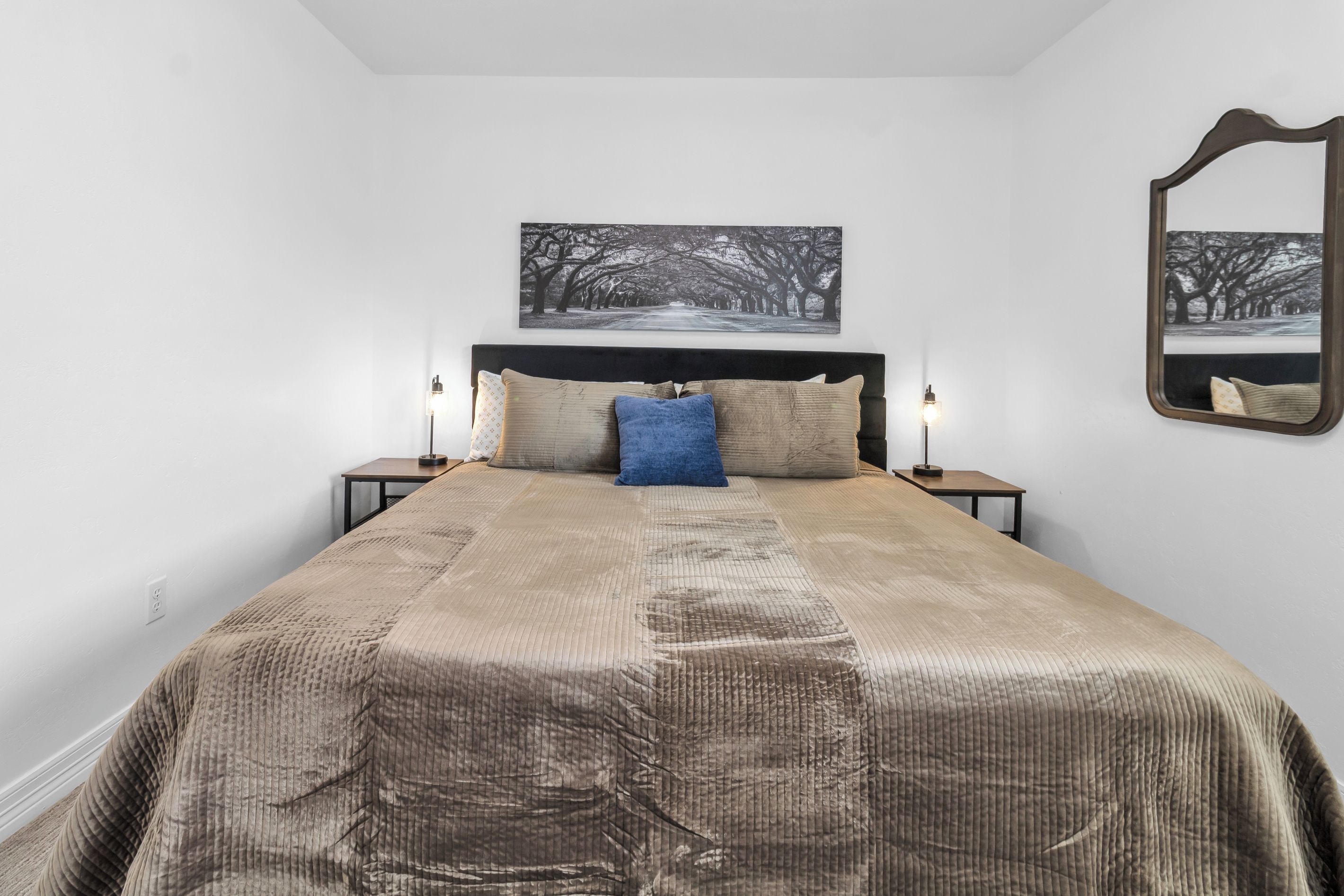 A bedroom with a large bed, two bedside tables, a wall-mounted mirror, and a framed picture above the bed.
