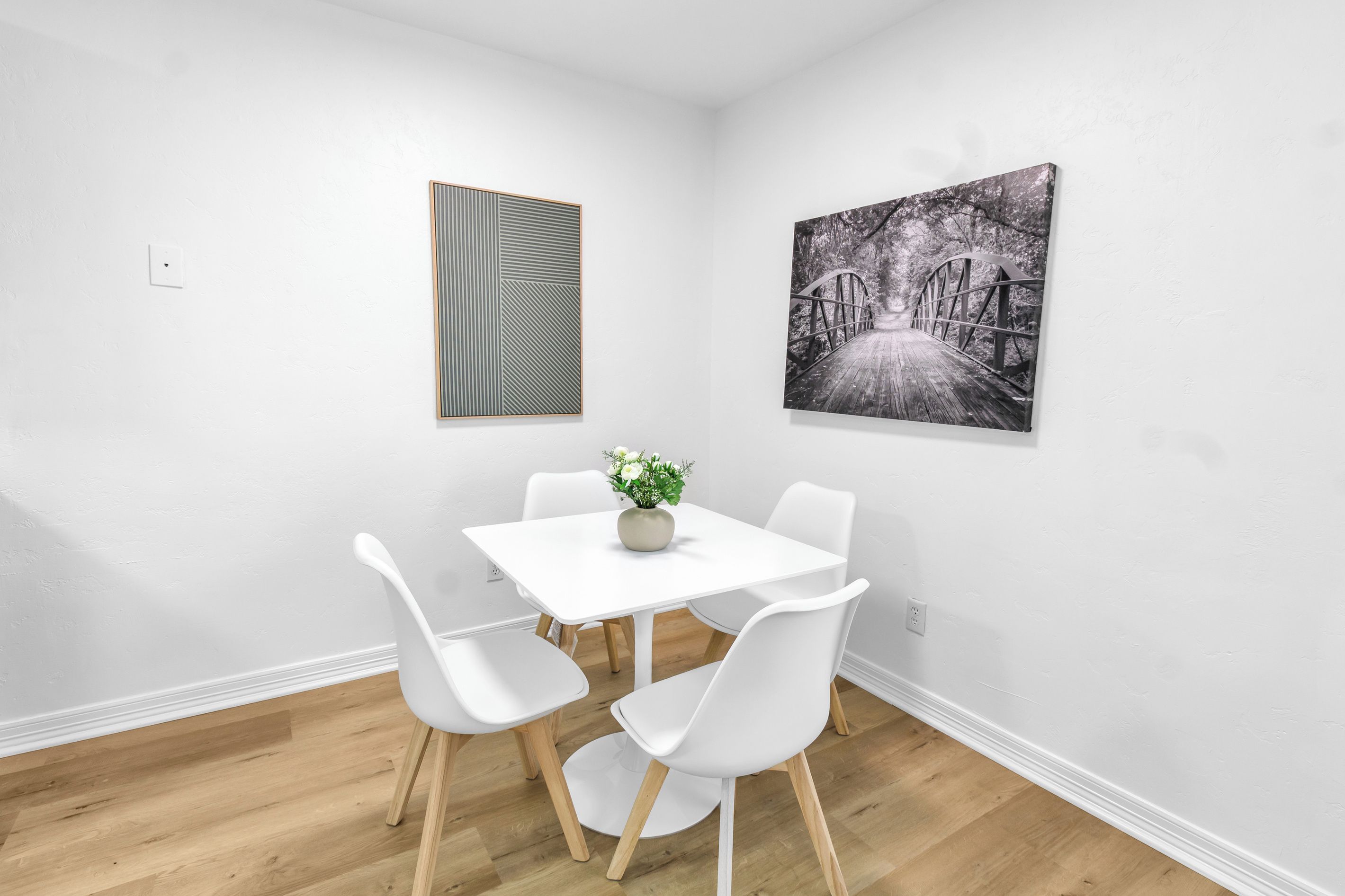 A room with a white table and chairs, a potted plant, and two wall-mounted artworks.