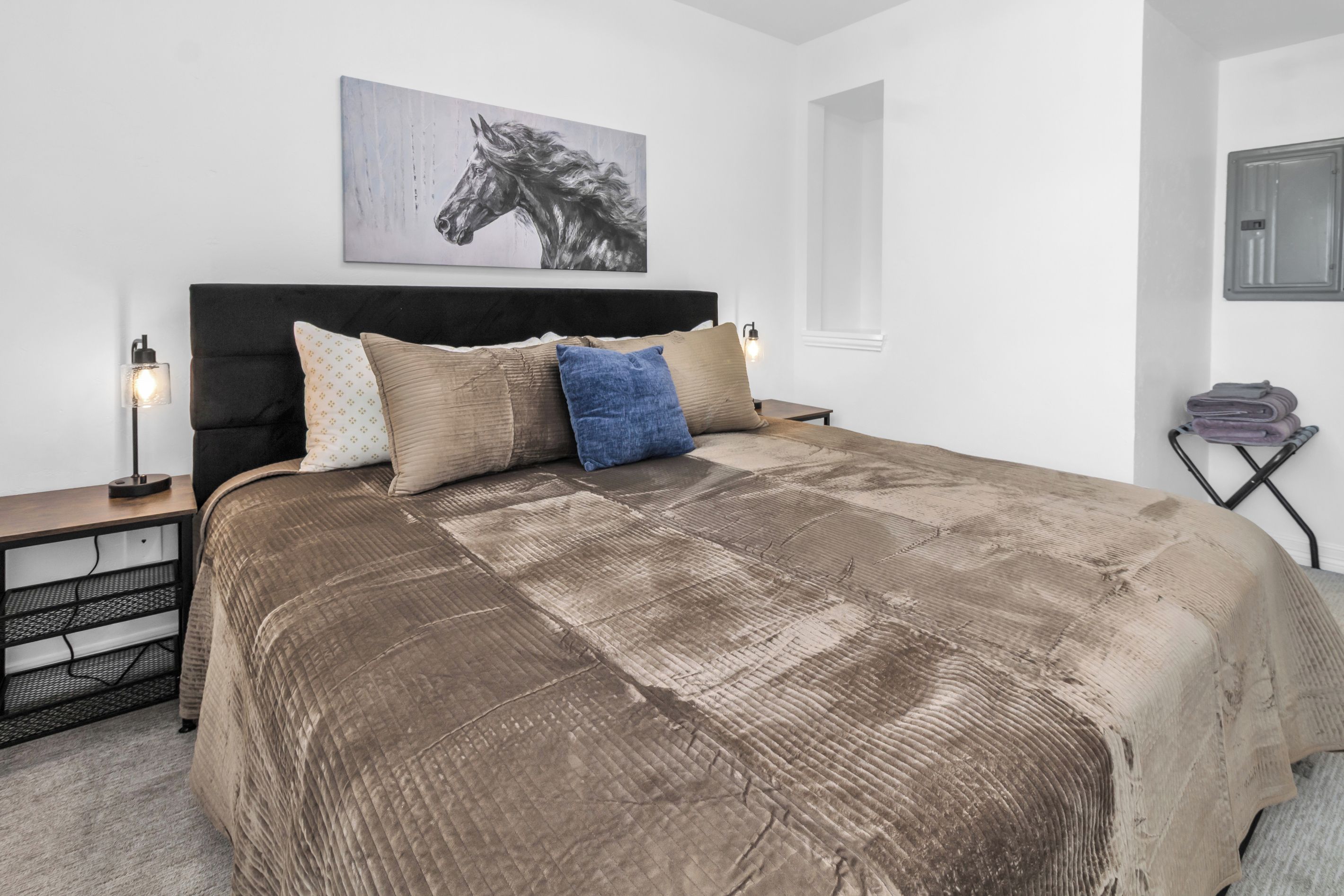 Une chambre à coucher avec un grand lit, une tête de lit, une table de chevet avec une lampe et une œuvre d’art accrochée au mur.