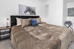 Un dormitorio con una cama grande, un cabecero, una mesita de noche con lámpara y una obra de arte colgada en la pared.