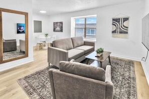 Una sala de estar moderna con un sofá, sillones, una mesa de centro y un comedor con una mesa y sillas.