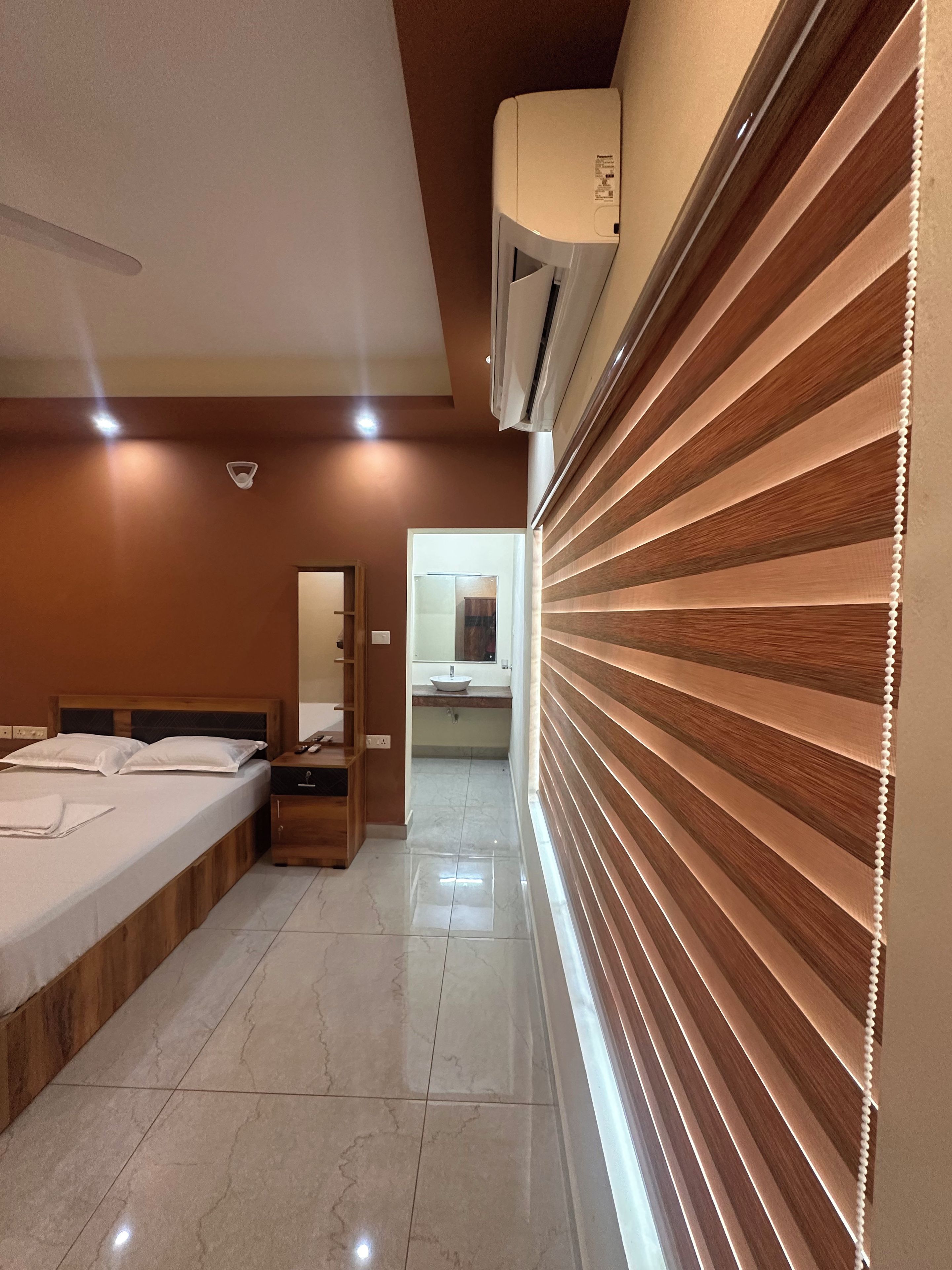 A hotel room with a bed, bedside table, and a mirror. There is a bathroom visible in the background.