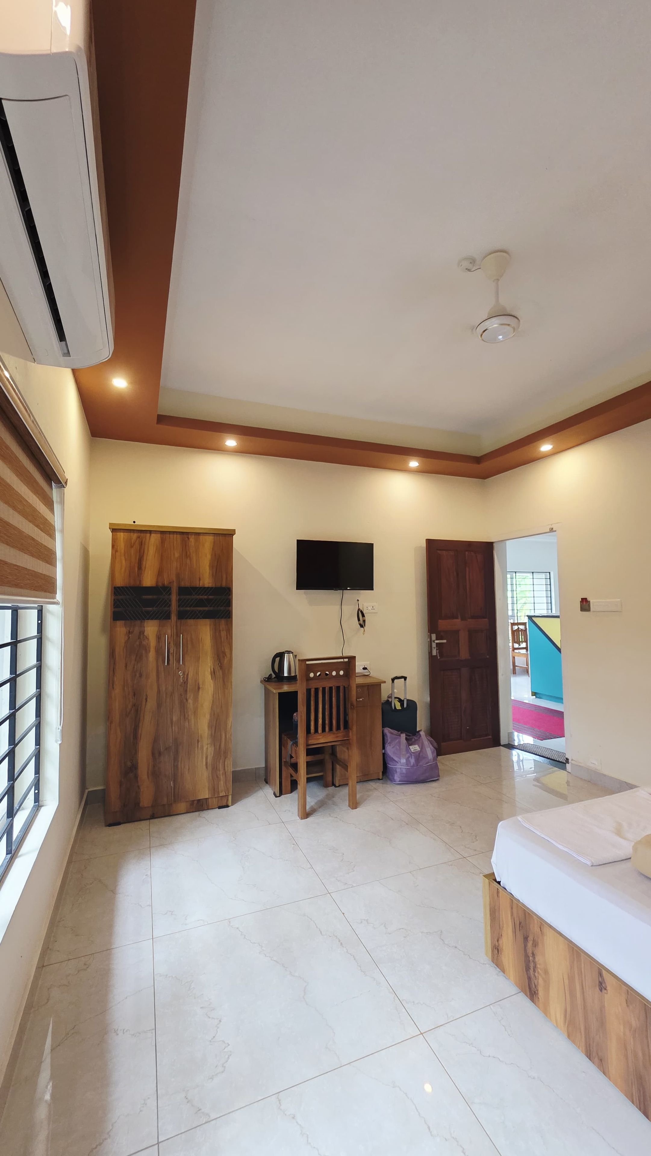 A bedroom with a bed, wardrobe, desk, chair, television, and a bathroom visible through an open door.