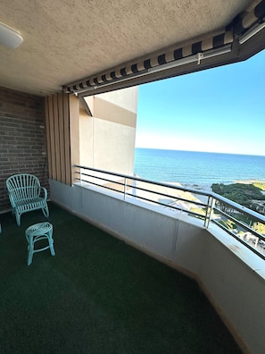 A balcony with a view of the sea, a brick wall, and two wicker chairs.