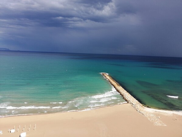 A beach with a long pier extending into the sea, clear turquoise water, and a sandy shore.
