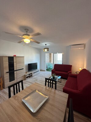 A modern living room with a television, red sofa, and a dining table with a tray.