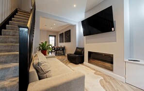 A modern living room with a staircase, a fireplace, a flat-screen TV, and a dining area with chairs and a table. - Cosy 2 bed tce - walk to city centre (Chester)