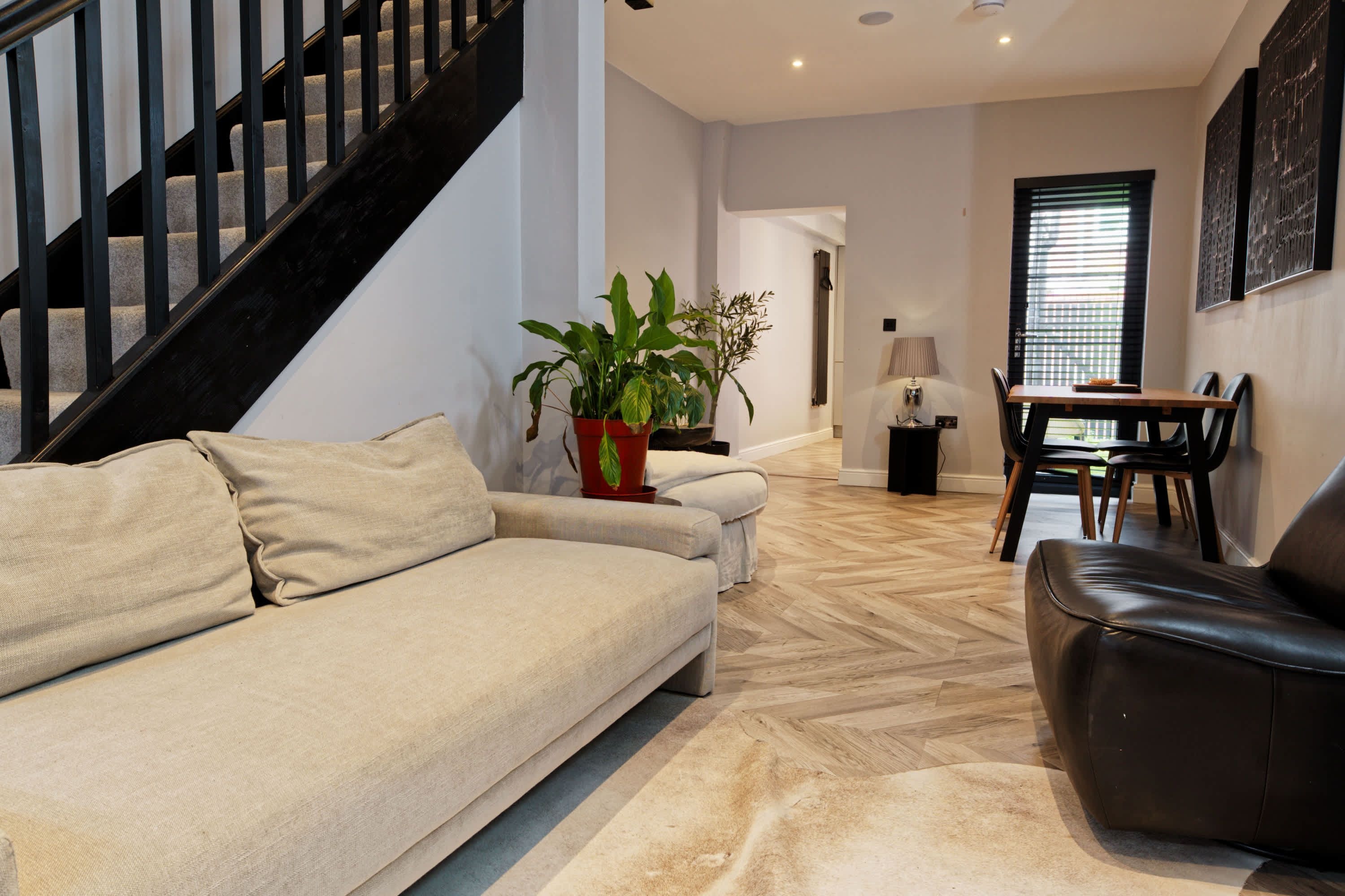 A modern living room with a sofa, a coffee table, a dining table with chairs, and a staircase.