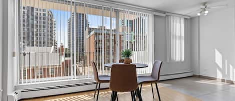 A modern living room with a large sliding glass door, a round table with chairs, a potted plant, and a ceiling fan.