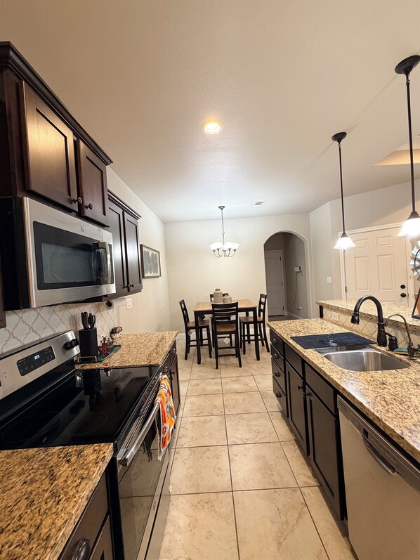 A modern kitchen with granite countertops, stainless steel appliances, and a dining area with a chandelier.