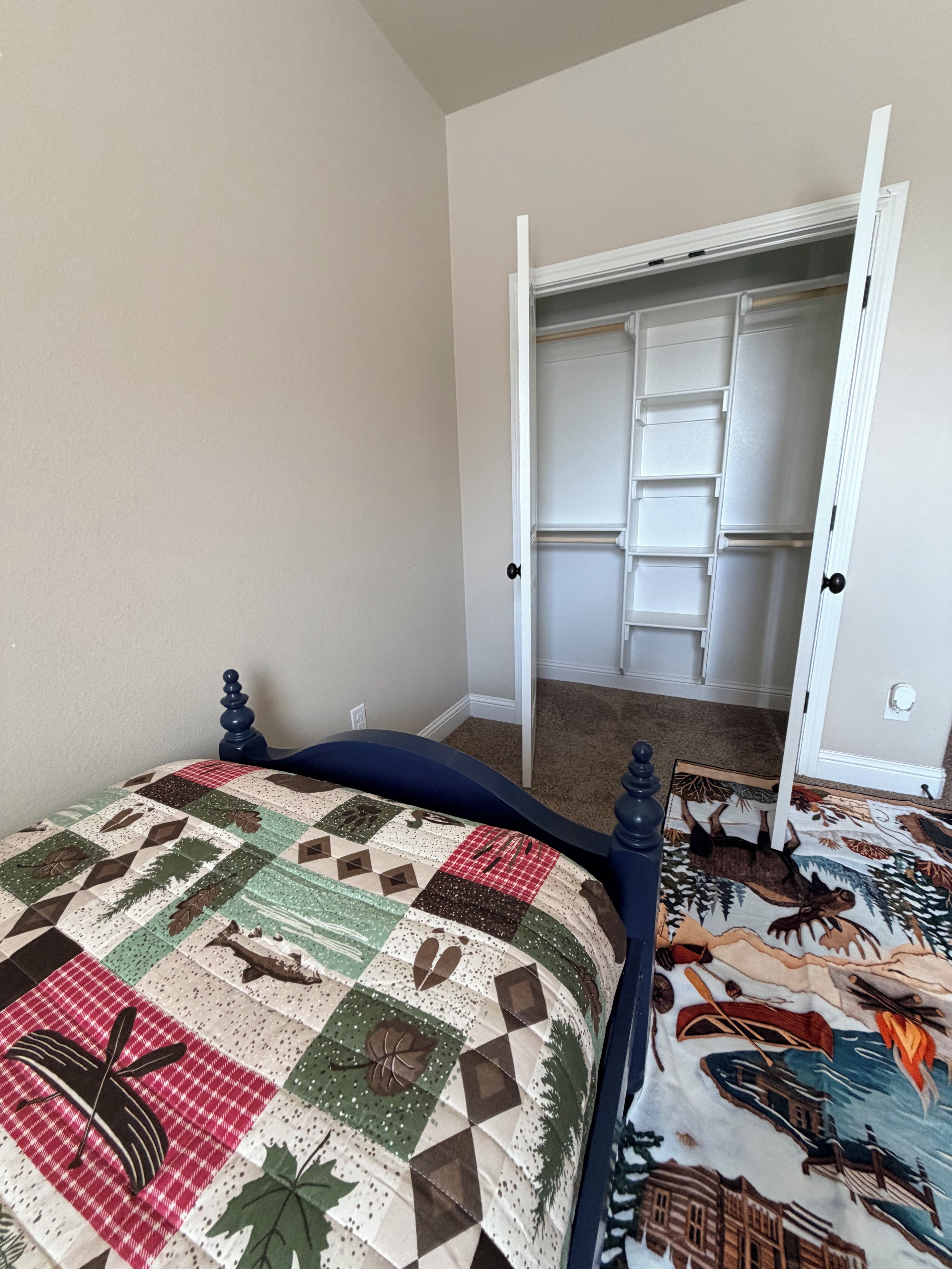 Un dormitorio con cama, armario abierto y suelo alfombrado.