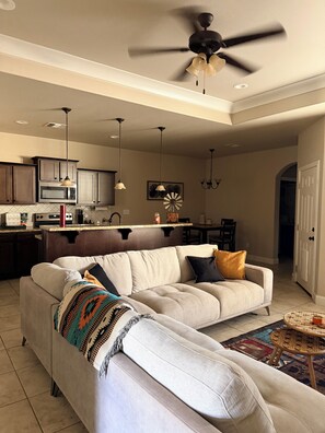 A modern living room with a sectional sofa, a dining area, and a kitchen.