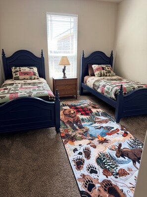 A bedroom with two beds, a nightstand, a lamp, and a rug with animal prints.
