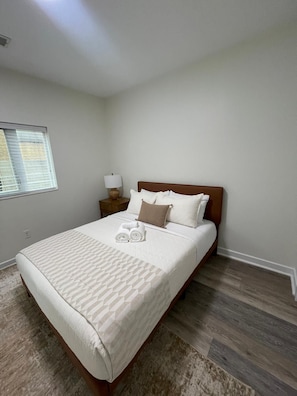 A neatly made bed with a patterned bedspread, a nightstand with a lamp, and a window with blinds. - Updated 2Bedroom with a pool and hot tub (Columbus)