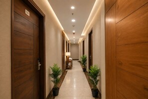 Un pasillo de hotel con puertas de madera, una mesa de recepción y plantas en macetas.