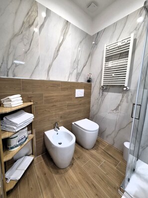 A modern bathroom with marble walls, a bidet, a toilet, and a shower area. - Elevin Apartments Bari (Bari)