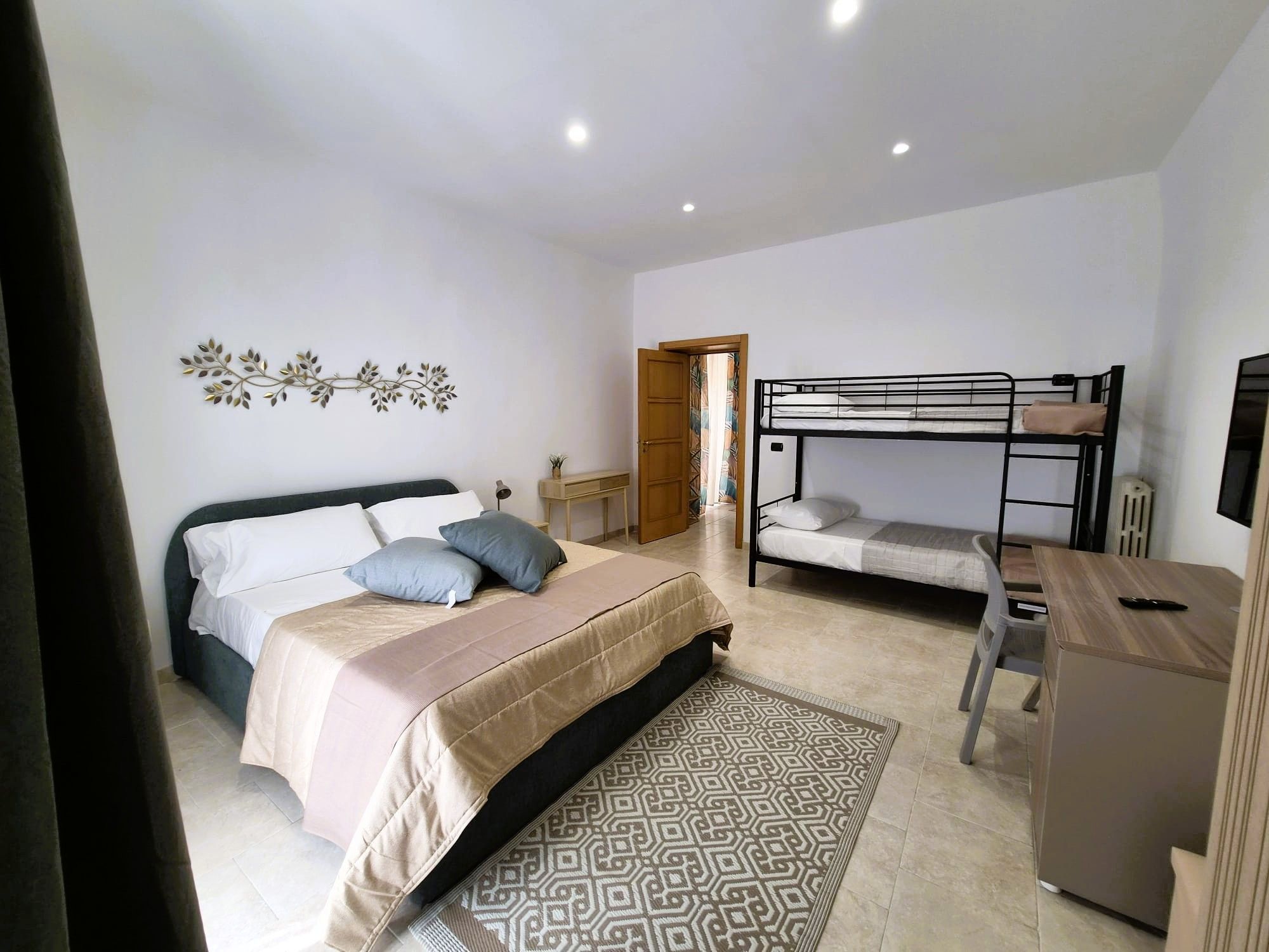 A bedroom with a bed, a bunk bed, a desk, and a decorative wall piece.
