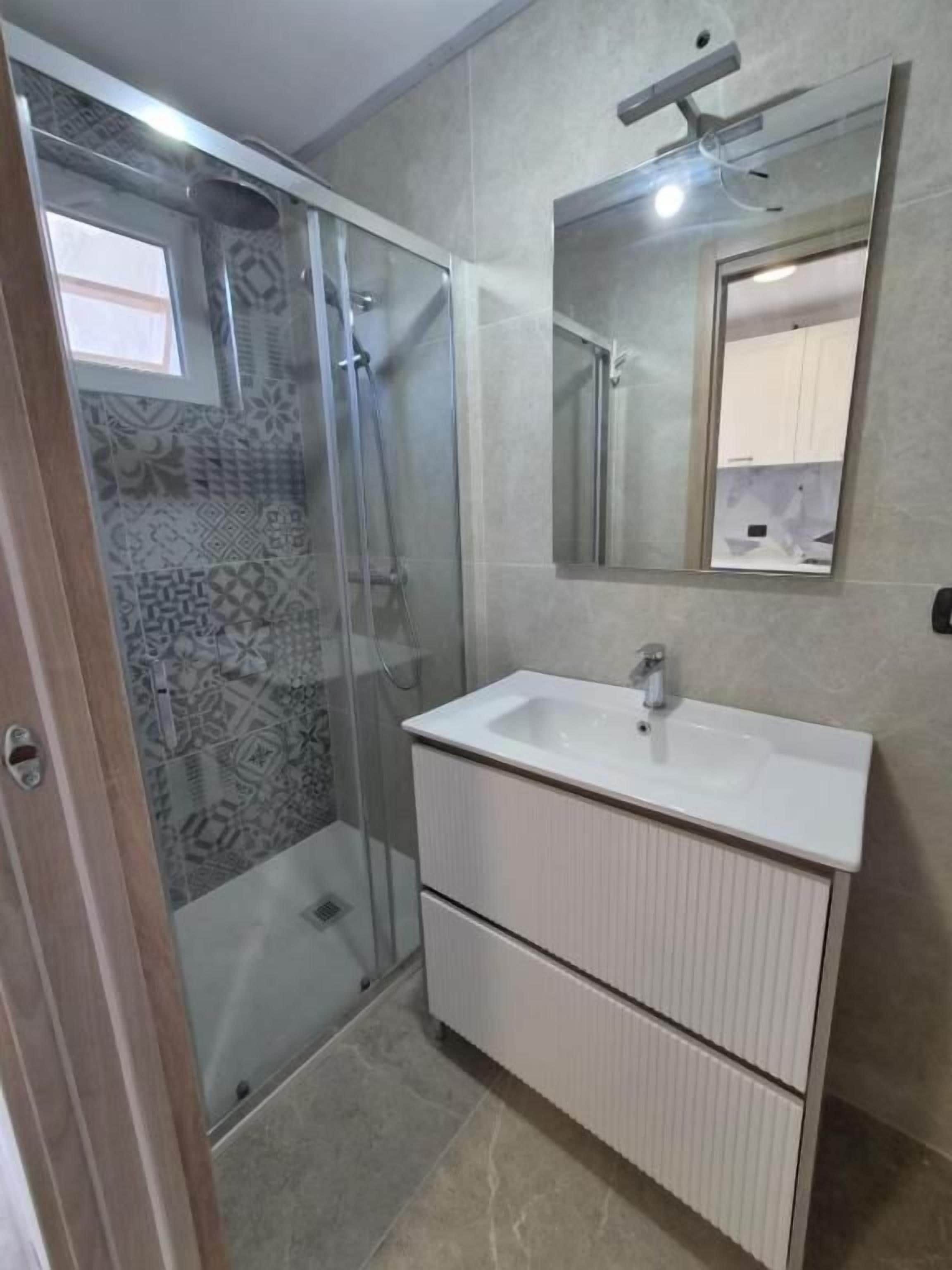 A bathroom with a glass-enclosed shower, a white sink, and a mirror above it.