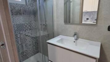 A bathroom with a glass-enclosed shower, a white sink, and a mirror above it.