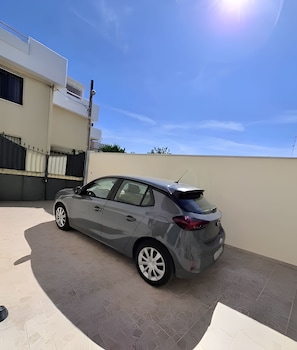 Un sedán gris estacionado en una entrada con cielo despejado.