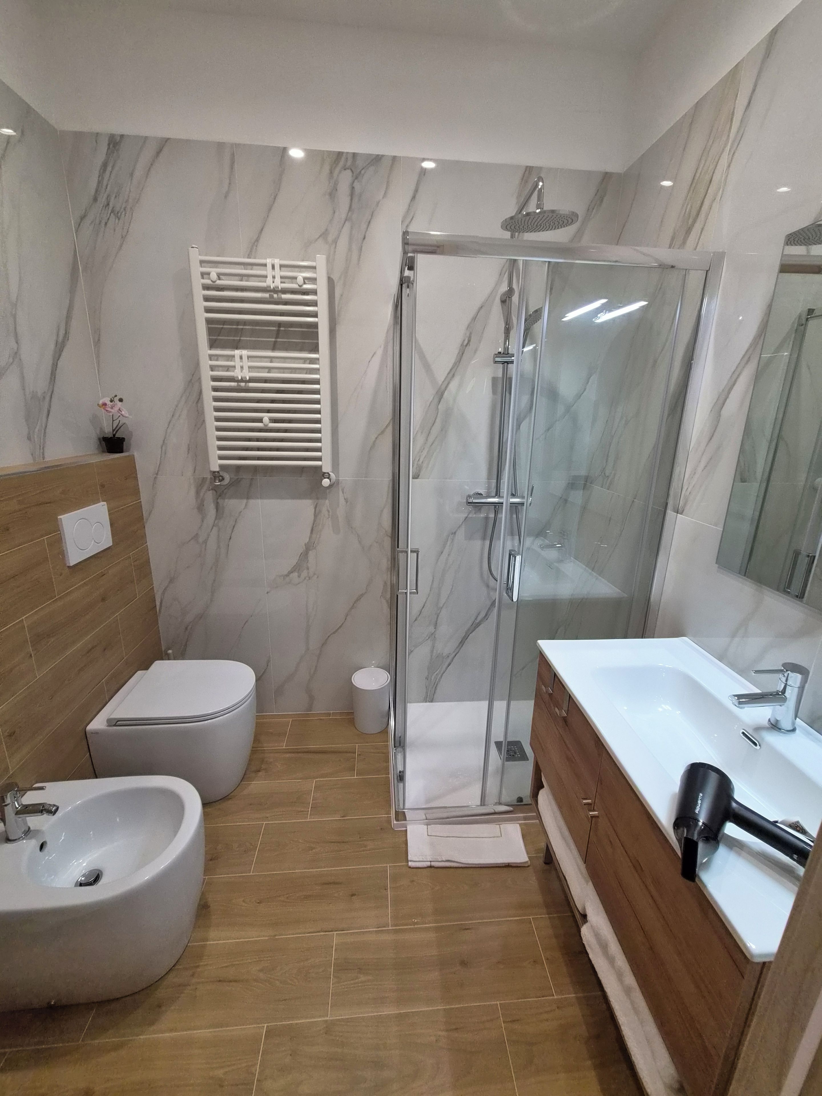 Casa de banho moderna com chuveiro em cabine de vidro, bidé, sanita e toucador com lavatório.