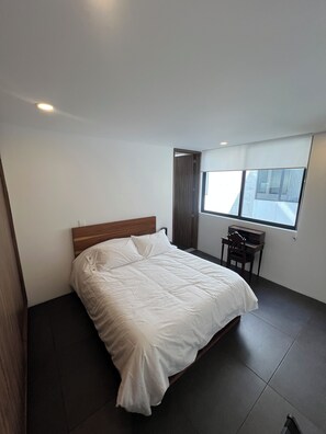 Un dormitorio con cama, escritorio y ventana.