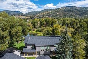A modern two-story house with a flat roof, surrounded by lush greenery and a lake. - Tranquil Riverfront Property Close to the Resort! Pet Friendly! (Steamboat Springs)