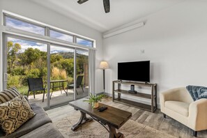 A living room with a sofa, coffee table, TV stand, and a view of a balcony with outdoor furniture. - Tranquil Riverfront Property Close to the Resort! Pet Friendly! (Steamboat Springs)