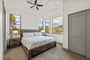 A bedroom with a bed, nightstands, a ceiling fan, and large windows with a view of the outdoors. - Tranquil Riverfront Property Close to the Resort! Pet Friendly! (Steamboat Springs)
