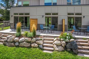 A modern building with a patio area featuring outdoor seating and a stone wall with plants. - Riverfront Condo Only 10 Minutes to the Resort! Pet Friendly. (Steamboat Springs)