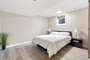 Ein Schlafzimmer mit einem Bett, Nachttischen, einer Zimmerpflanze und einem Fenster mit Jalousien.