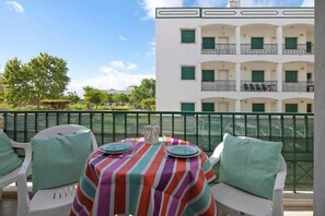 Un espacio al aire libre con una mesa dispuesta para dos, sillas blancas y vistas a un edificio con balcones.