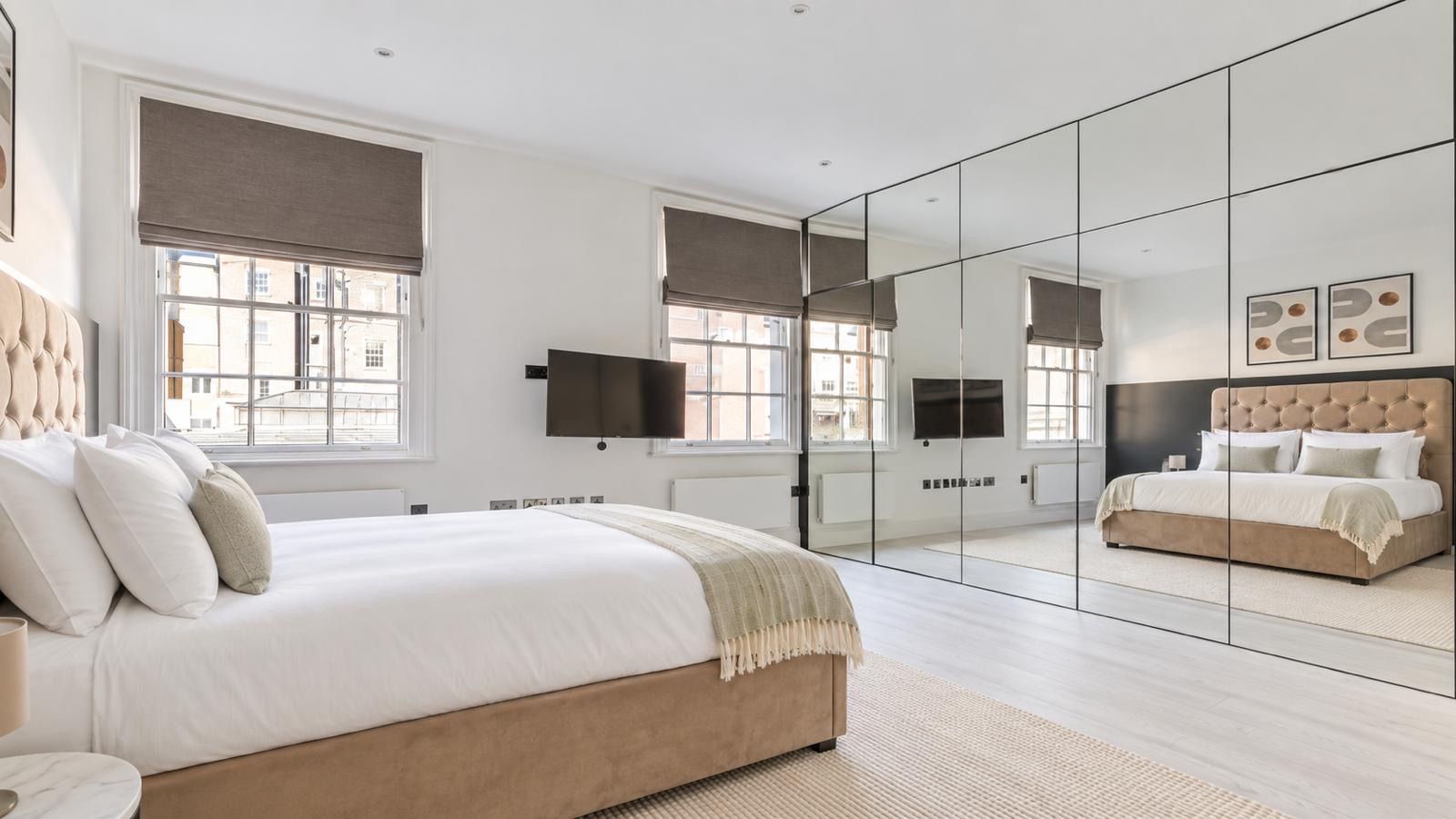Een moderne slaapkamer met een groot bed, een televisie en een spiegelwand.