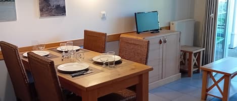 Ein Essbereich mit einem Holztisch, gedeckt für vier Personen, umgeben von Korbstühlen, einer schwarzen Pendelleuchte und einer Wandlampe.