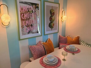 Een eetgedeelte met een gedekte tafel voor twee, kunstwerken aan de muur en decoratieve kussens.