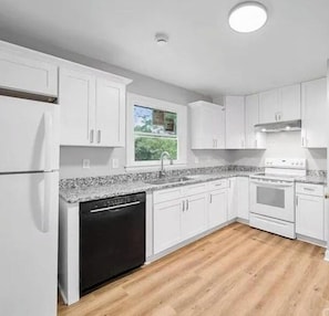 A kitchen with white cabinets, a dishwasher, a stove, and a window with a view of greenery. - The Slide House - Theater - Hot Tub - Sleep 12 (Charlotte)