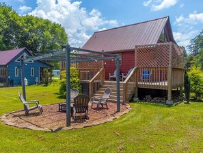 A wooden deck with outdoor furniture, a covered area with stairs, and a red building with a metal roof. - Bearfoot Bliss ~ Bryson City Cabin: Hot Tub & Mountain Escape (Bryson City)