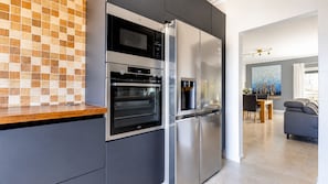 Een moderne keuken met een inbouwoven en koelkast, een houten aanrecht en een eethoek met tafel en stoelen.