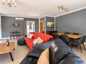 Een moderne woonkamer met een rode bank, een zwarte leren fauteuil en een houten eettafel met stoelen.