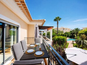 Ein Balkon mit Esstisch für zwei Personen, ein Pool im Hintergrund und Blick auf die umliegenden Gebäude.