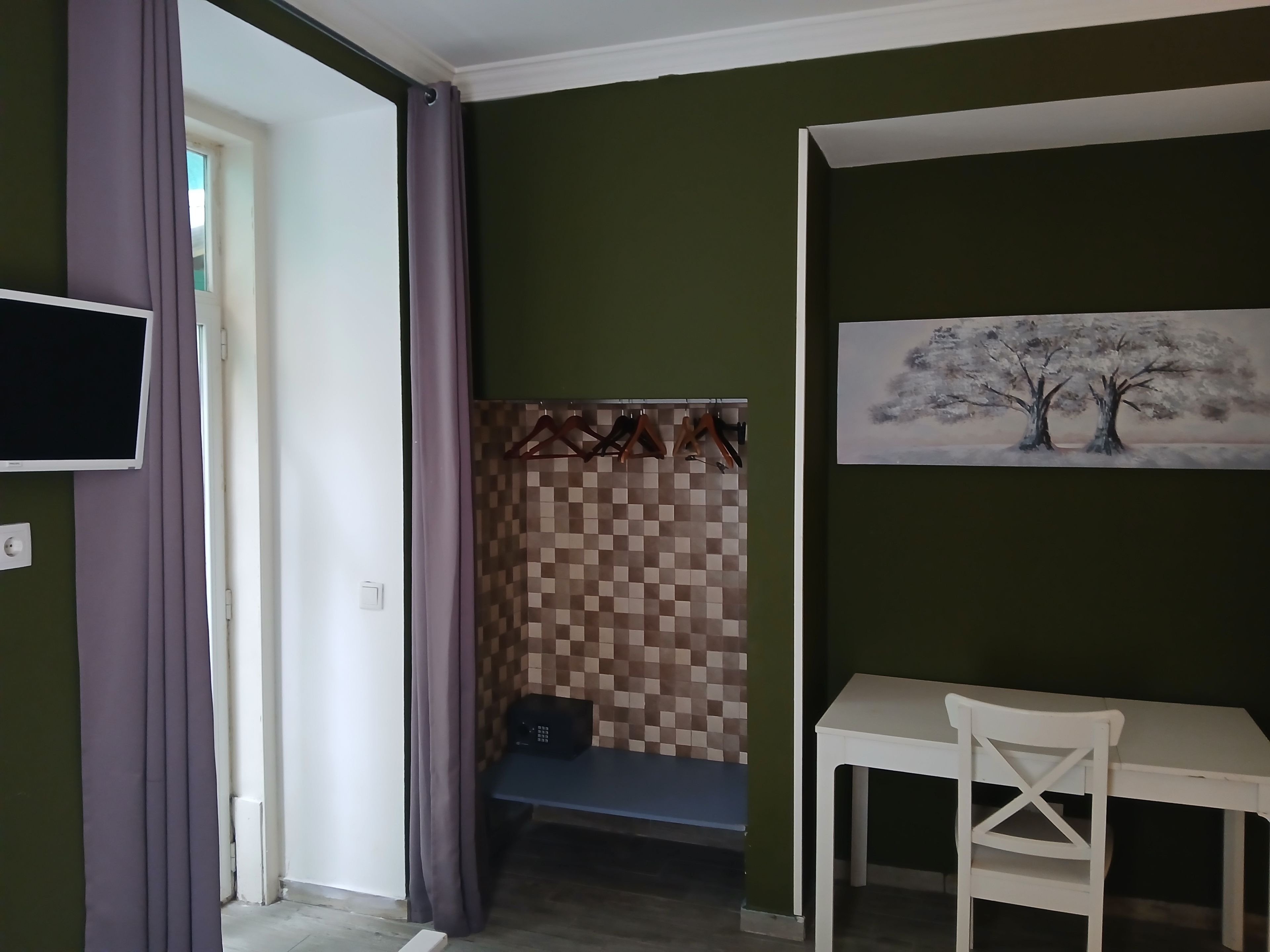 A room with a television, a painting of trees, a table, and a bench.