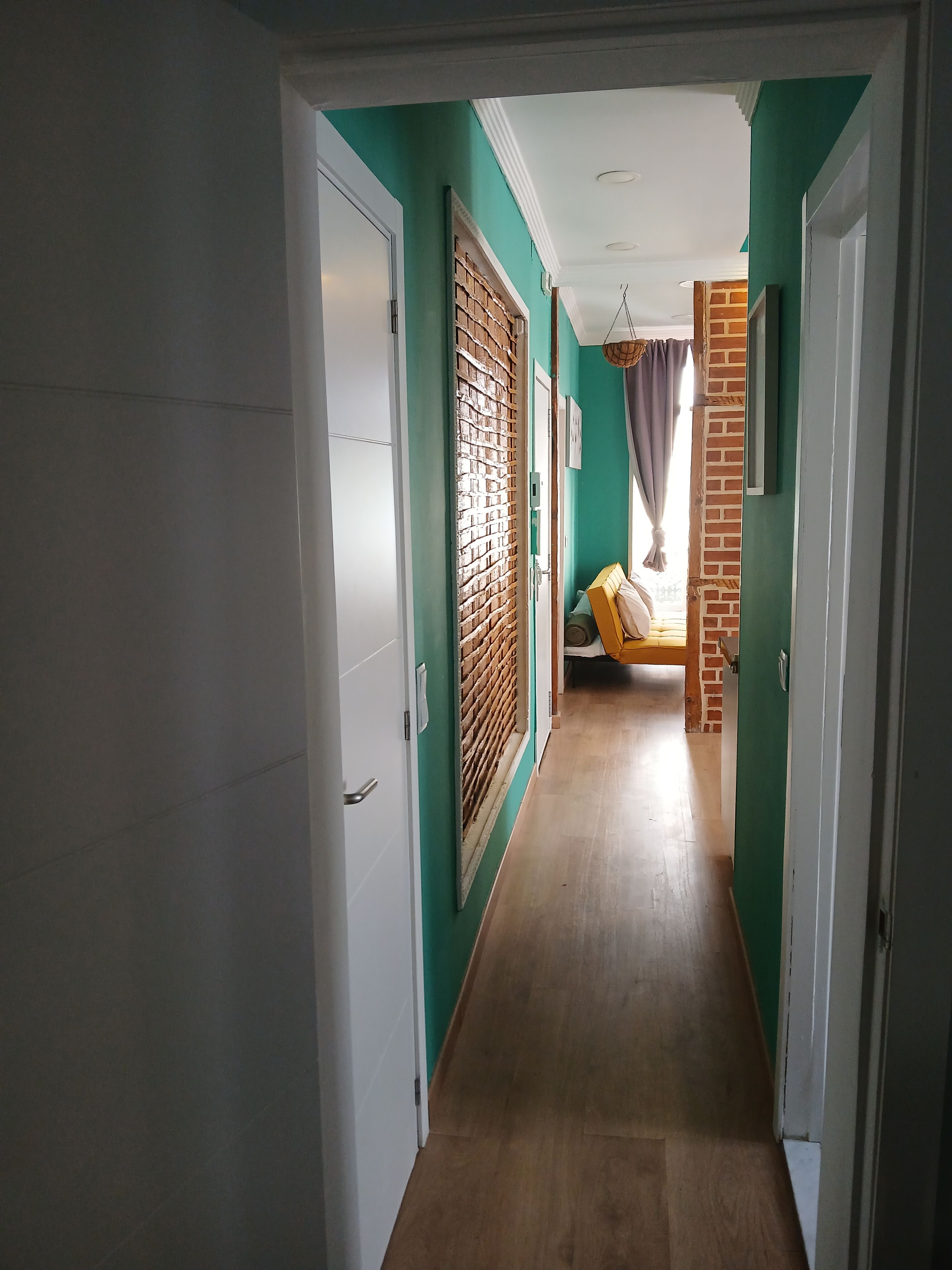 A hallway with a wooden floor, green walls, and a bed with a yellow headboard.