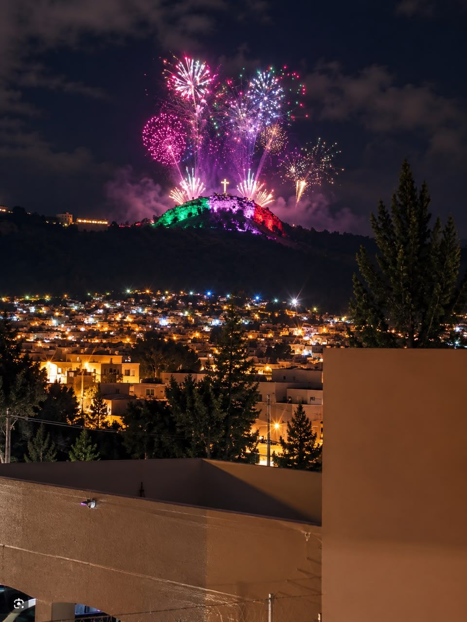 Vista nocturna de un pueblo con una colina al fondo.