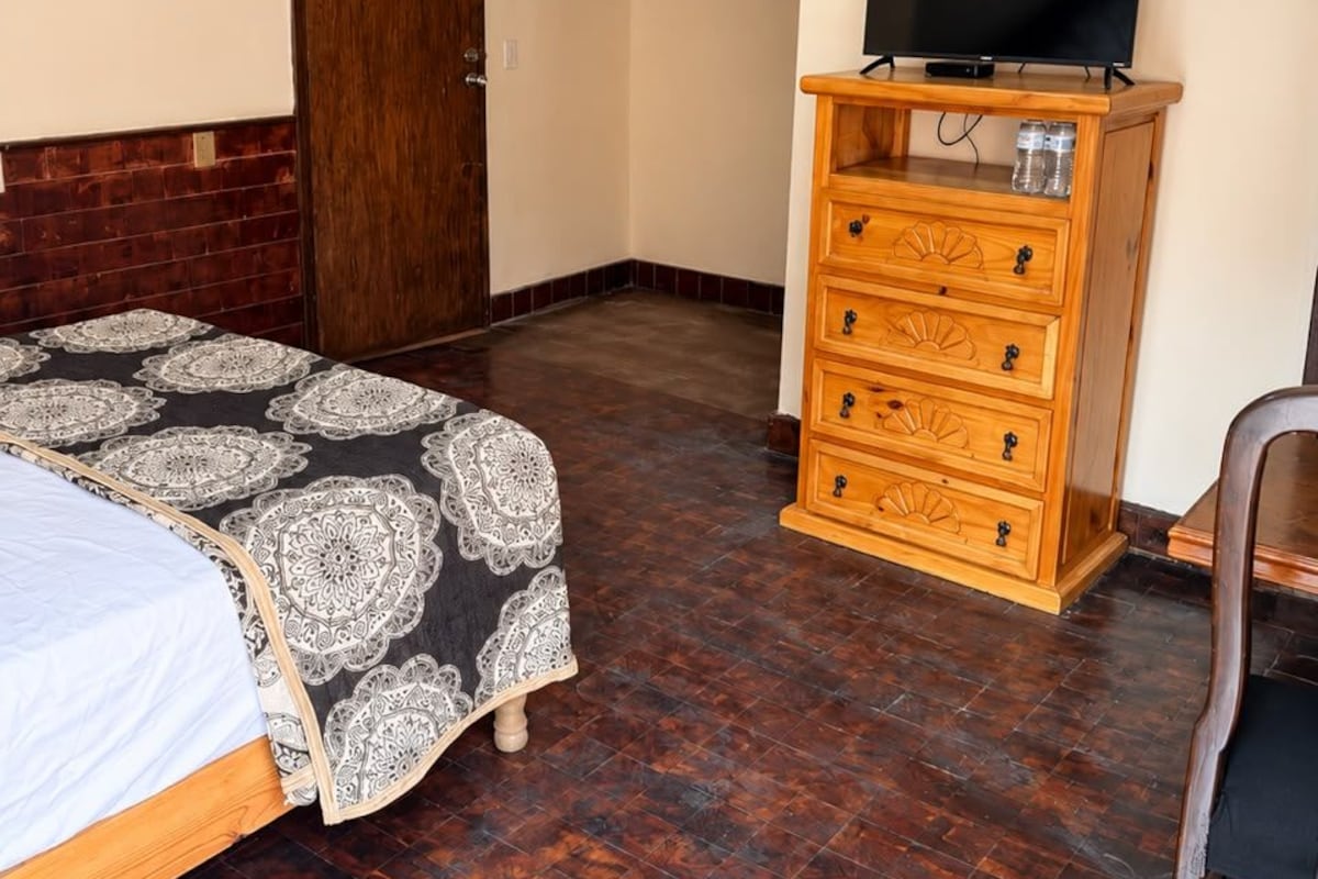 A room with a bed, a wooden dresser, a television, and a door.
