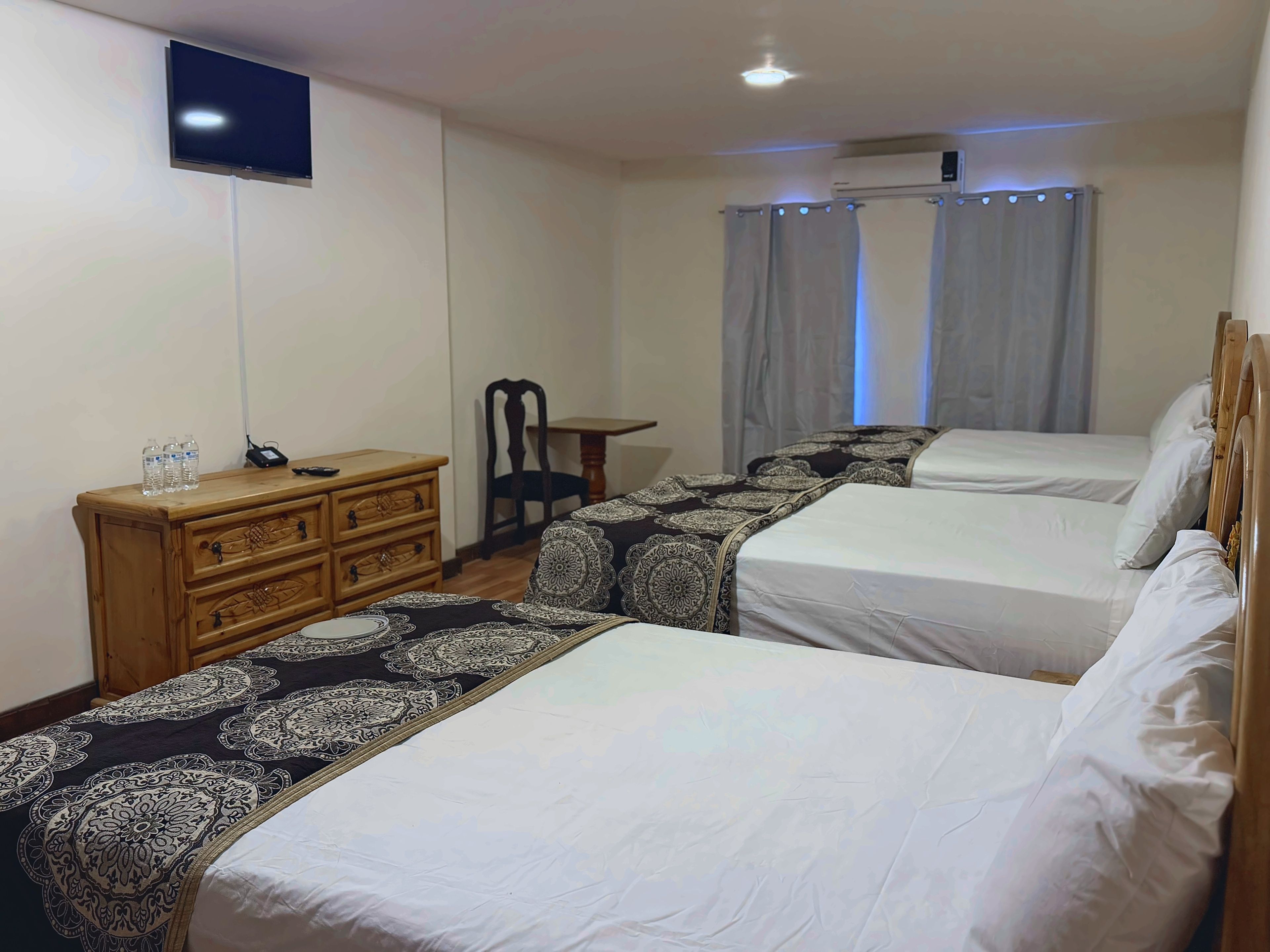 A hotel room with two beds, a wooden dresser, a flat-screen TV, and a table.